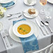 A table set with a bowl of soup and silverware, including an Acopa Ophelia stainless steel fork.