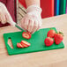 A person cutting strawberries on a green Choice cutting board.