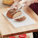 A person cutting bread on a Choice white polyethylene cutting board.