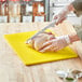 A person cutting a chicken on a yellow Choice polyethylene cutting board.