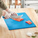 A person cutting a piece of meat on a blue Choice cutting board.