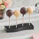 An Acopa black wood skewer stand holding cake pops on a table in a bakery display.