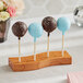 An Acopa dark brown wood skewer/cake pop holder with three cake pops on a table.