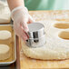 A hand using a Choice stainless steel round cookie cutter to cut dough.