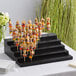 An Acopa black wood skewer holder with food on it.