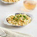 A Choice stainless steel round au gratin dish with macaroni and cheese on a plate with a fork.