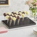An Acopa black wood skewer holder with chocolate covered cake pops on a table.