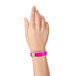 A woman's hand wearing a neon pink Carnival King wristband.