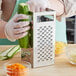 A person grating a cucumber with a Choice box grater over a bowl.