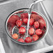 A stainless steel Chinese colander filled with red potatoes being washed under a faucet.