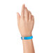 A person's hand with a Carnival King neon blue disposable plastic wristband.