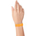A close-up of a hand holding a neon orange Carnival King wristband.