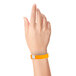 A person holding a neon orange Carnival King wristband with a silver button.