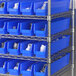 A metal shelf with blue Regency shelf bins filled with white containers.