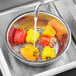 A Choice stainless steel Chinese colander filled with yellow bell peppers under running water.