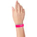A close-up of a hand wearing a neon pink Carnival King wristband.