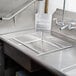 A stainless steel Advance Tabco pre-rinse basket with a welded slide bar over a stainless steel sink with a faucet.