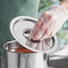 A person wearing a plastic glove putting a Choice stainless steel bain marie cover on a pot of food.