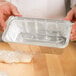 A hand pouring dough into a D&W aluminum foil loaf pan.