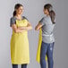 Two women wearing Choice yellow vinyl aprons standing in a professional kitchen.