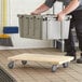 A man using a Lavex solid wood dolly to move a grey plastic container.