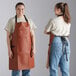 Two women wearing Choice light brown vinyl aprons with brown leather straps.