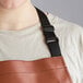 A woman wearing a light brown vinyl restaurant apron with a black strap.