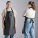 Two women wearing black Choice heavy weight vinyl aprons and jeans on a counter in a professional kitchen.