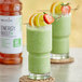 A green smoothie with strawberries and orange slices on a table with a Monin Energy Boost label.