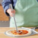 A person holding a stainless steel flat bottom ladle over a pizza.