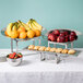 An American Metalcraft stainless steel display riser set on a table with bowls of fruit.