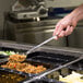 A person holding a Choice 15" Solid Stainless Steel Basting Spoon over food