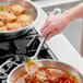 A hand using a Choice stainless steel basting spoon to stir food in a pan.