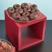 A table in a bakery display with a plate of chocolate donuts on a mahogany wood riser.