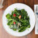A CAC Golden Royal bright white porcelain plate with a spinach salad with nuts and strawberries.