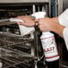 A person cleaning an oven with Noble Chemical Blast Ready-to-Use Liquid Oven & Grill Cleaner.