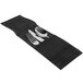 A black woven vinyl silverware pocket with a knife and fork on a black place mat.