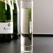 A Libbey flute glass filled with white liquid next to champagne bottles.