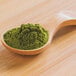 A spoonful of Moringa Powder on a wooden table.