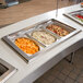 A row of Vollrath stainless steel decorative steam table pans filled with food on a buffet counter.