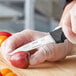 A person in gloves uses a Schraf Smooth Edge Paring Knife to cut a tomato.