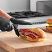 A person in black gloves using a Schraf serrated curved bread knife to cut a sandwich.