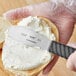 A person uses a Schraf scalloped sandwich spreader to spread cream cheese on a bagel.