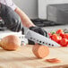 A person in gloves uses a Schraf 8" vegetable knife to cut up a large round vegetable on a cutting board.