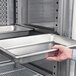 A hand using Avantco shelf rails to hold a tray in a refrigerator.