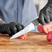 A hand in a black glove uses a Schraf serrated knife to cut a tomato.