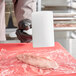 A person in gloves using an Omcan plastic meat tenderizer on a piece of meat.