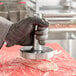 A person in a black glove using an Omcan stainless steel meat tenderizer.