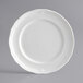 An Acopa Condesa porcelain plate with a decorative scalloped edge on a gray background.