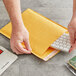 A hand using a keyboard to open a yellow Lavex Self-Sealing Kraft Bubble Mailer.